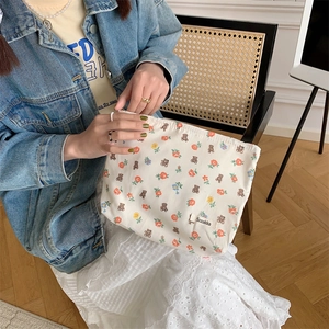 Floral makeup bag with bear pattern and brand label held by a model in a cozy indoor setting
