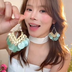 Detail of elegant gold earrings with green round pendants and pearl tassel on a model