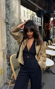 Giacca in tweed con paillettes dorate sopra un outfit nero in un caffè di Parigi
