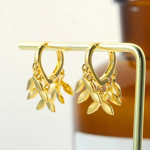 Detail of golden leaf dangle earrings featuring heart hooks on a minimalist jewelry stand