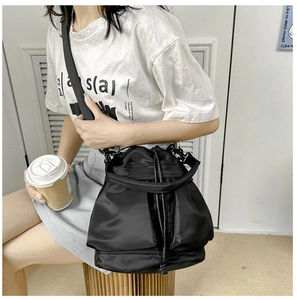 Detail van zwarte nylon bucket bag met trekkoord en brede schouderband op het model