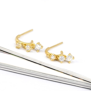 Macro detail of gold earrings with three-stone zircon inlay and minimalist drop design