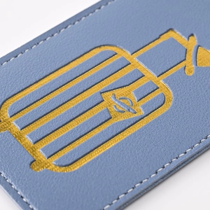 Close-up of blue PU leather luggage tag with golden birdcage embossing and textured finish