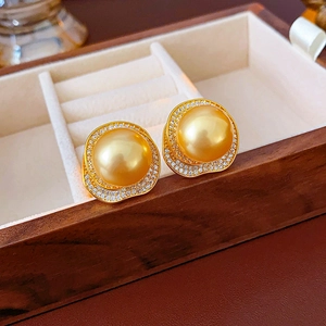 Macro shot of gold pearl stud earrings with zircon petals in a wooden jewelry box