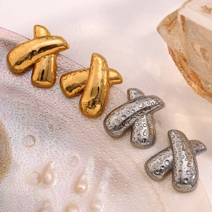 Close-up of geometric X-shaped stud earrings in gold and silver with water droplets