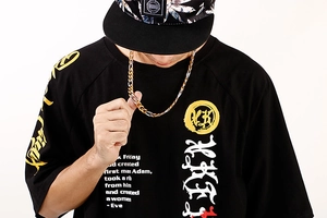 Gros plan d'une personne portant une chaîne Figaro 3:1 dorée style hip-hop sur un t-shirt noir