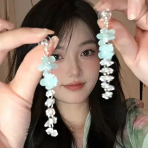 Detailed view of light blue acrylic flower tassel earrings with silver chains on model