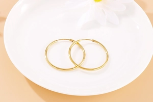 Detailed view of polished golden 304 stainless steel hoop earrings on a ceramic dish