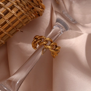 Detailed view of a gold braided Cuban chain ring on pink silk with a glass backdrop