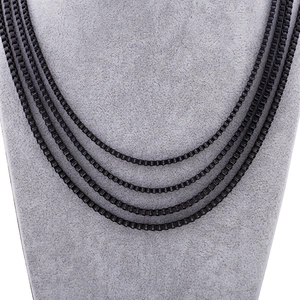 Detail of four black stainless steel box chains on a grey velvet mannequin display
