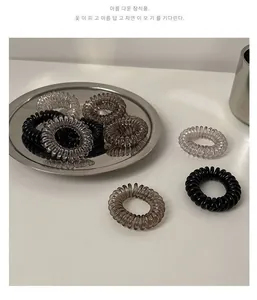 Macro detail of spiral elastic hair ties in neutral black and grey tones on steel tray