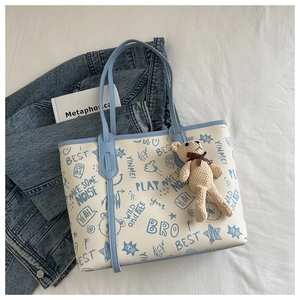 Close-up of graffiti tote bag with blue trim, knit bear charm and urban street art print