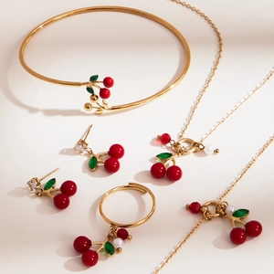 Gouden kersen sieradenset met rode kralen, ketning, armband, oorbellen en ring op beige