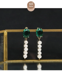 Detail of elegant gold drop earrings with deep green gemstones and white pearls