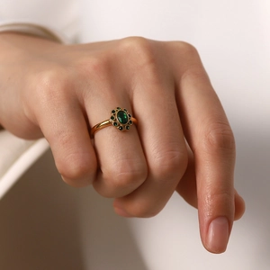 Close-up of gold ring with oval emerald gemstone and halo diamonds on finger