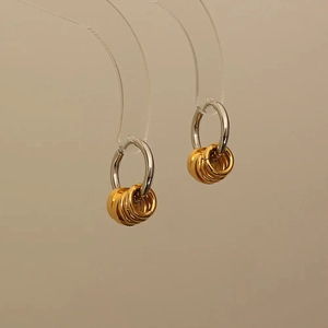 Detailed macro view of two-tone hoop earrings with silver main ring and gold charms
