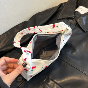 Floral nylon shoulder bag with cherry pattern and zipper closure shown on black jacket