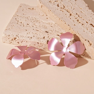 Detailed close-up of matte pink metal flower earrings on a textured stone surface