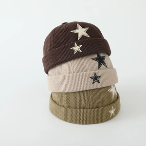Close-up of stacked corduroy sailor hats with star patches in brown, beige and green colors