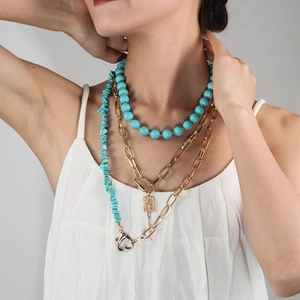 Detailed view of layered gold chain necklaces with turquoise beads on a model's neck