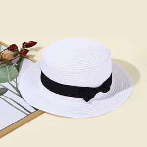Close-up of white flat top straw hat with black bow ribbon on a minimalist aesthetic background