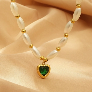 Detail of a heart-shaped green crystal pendant with gold rim and faux pearl necklace