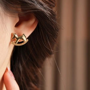 Detail of gold horse stud earrings with zircon on model ear with natural lighting