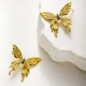 Detailed macro view of 3D gold butterfly stud earring with embossed texture and dark gemstone