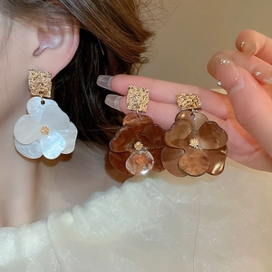 Macro view of acrylic flower earrings with golden wrinkled metal studs in white and amber