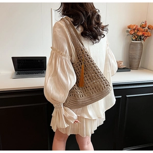 Brown woven shoulder bag with tassel detail worn by model in a minimalist indoor setting