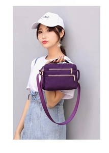 Detail of purple nylon crossbody bag with three golden zippers and adjustable strap