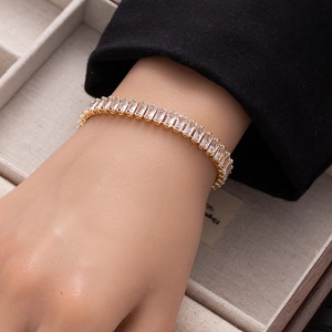 Detail shot of a gold tennis bracelet featuring rectangular white zircons on a wrist