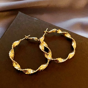 Macro detail of gold-plated twisted texture hoop earrings with elegant spiral pattern