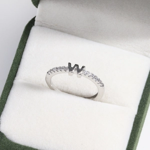 Macro view of adjustable silver letter W ring with small diamonds in a velvet box