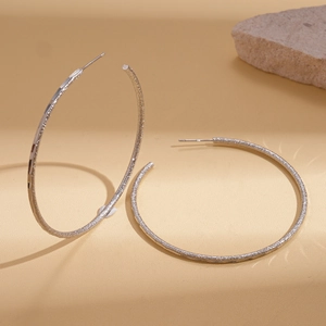Detailed close-up of large matte silver hoop earrings with a fine glitter texture finish