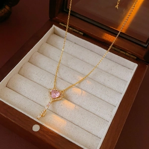 Detail of a gold key pendant necklace featuring a pink heart stone in a wooden jewelry box
