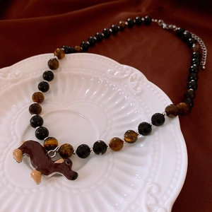 Close-up of a beaded tiger eye necklace with a brown dachshund pendant on a white tray
