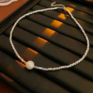 Detail of silver metallic gravel necklace featuring a large white pearl center on black tray