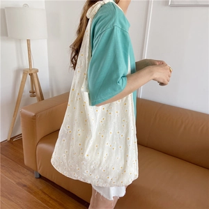 Daisy print white canvas tote bag shown on shoulder in a cozy home setting