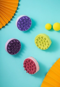 Flat lay of colorful silicone scalp massagers in purple, yellow, and pink on blue background