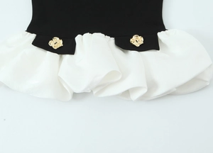 Detail of black patchwork top featuring white ruffled hem and ornate gold flower buttons