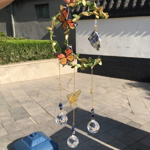 Detail of moon-shaped wind chime with green leaves, orange butterflies and crystal ball