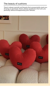 Red heart-shaped plush pillow with Happy Home label on a soft bouclé sofa