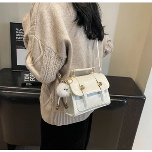 Side view of white PU leather crossbody bag with gold hardware and plush pendant on model
