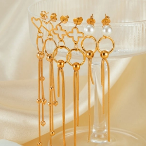 Detailed close-up of three gold tassel earrings featuring hearts, crosses, and pearls
