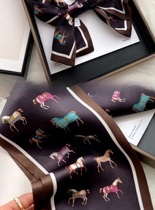 Detailed view of dark brown silk scarf with colorful horse pattern in luxury gift box