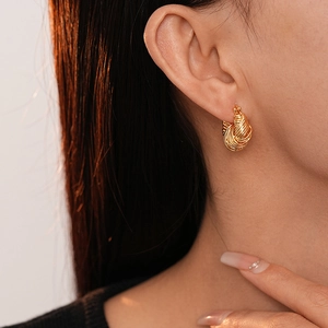 Close-up of gold-plated U-shaped earrings with twisted texture worn by a model