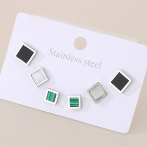 Close-up of three pairs of square stainless steel stud earrings in black, white, and green
