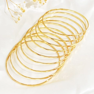 Set of 10 golden hammered metal bangles displayed on white silk fabric background