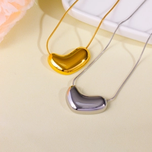 Golden and silver heart bean pendant necklaces with snake chains on ceramic tray